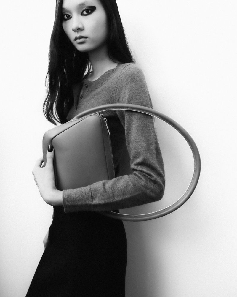 Monochrome portrait of an Asian fashion model in a studio. She is holding a handbag with a round handle, showcasing contemporary style.