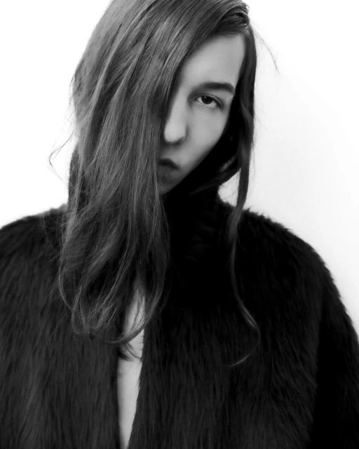 Black and white portrait of a young adult woman with long hair partially obscuring her face, wearing a dark, soft jacket.