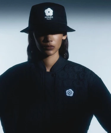Model wearing a black bucket hat and quilted jacket with white boke flower logos against a pale background