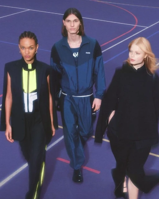 Three fashion models pose indoors on a blue court wearing athleisure outfits in black and blue. The models face the camera.