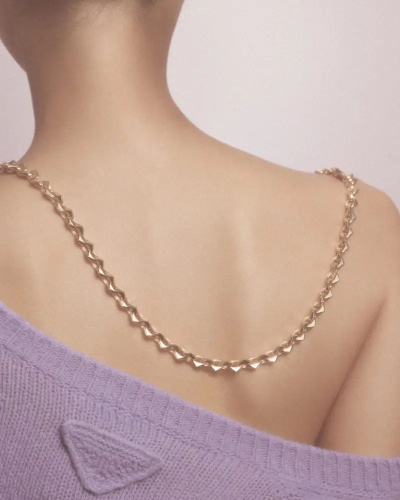 Close-up of fair-skinned woman's bare back and shoulders, adorned with a gold-colored chain necklace, and wearing a lavender sweater.