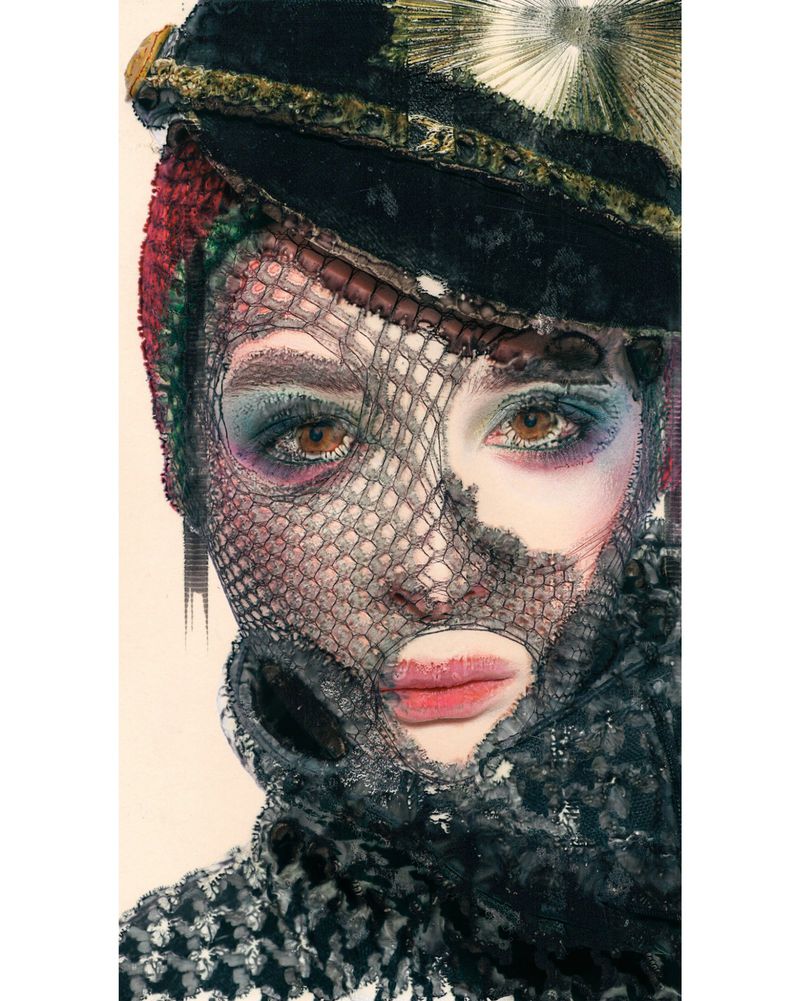 Artistic portrait of a person with elaborate makeup, headwear, and a veil in a close-up studio shot against a plain background.
