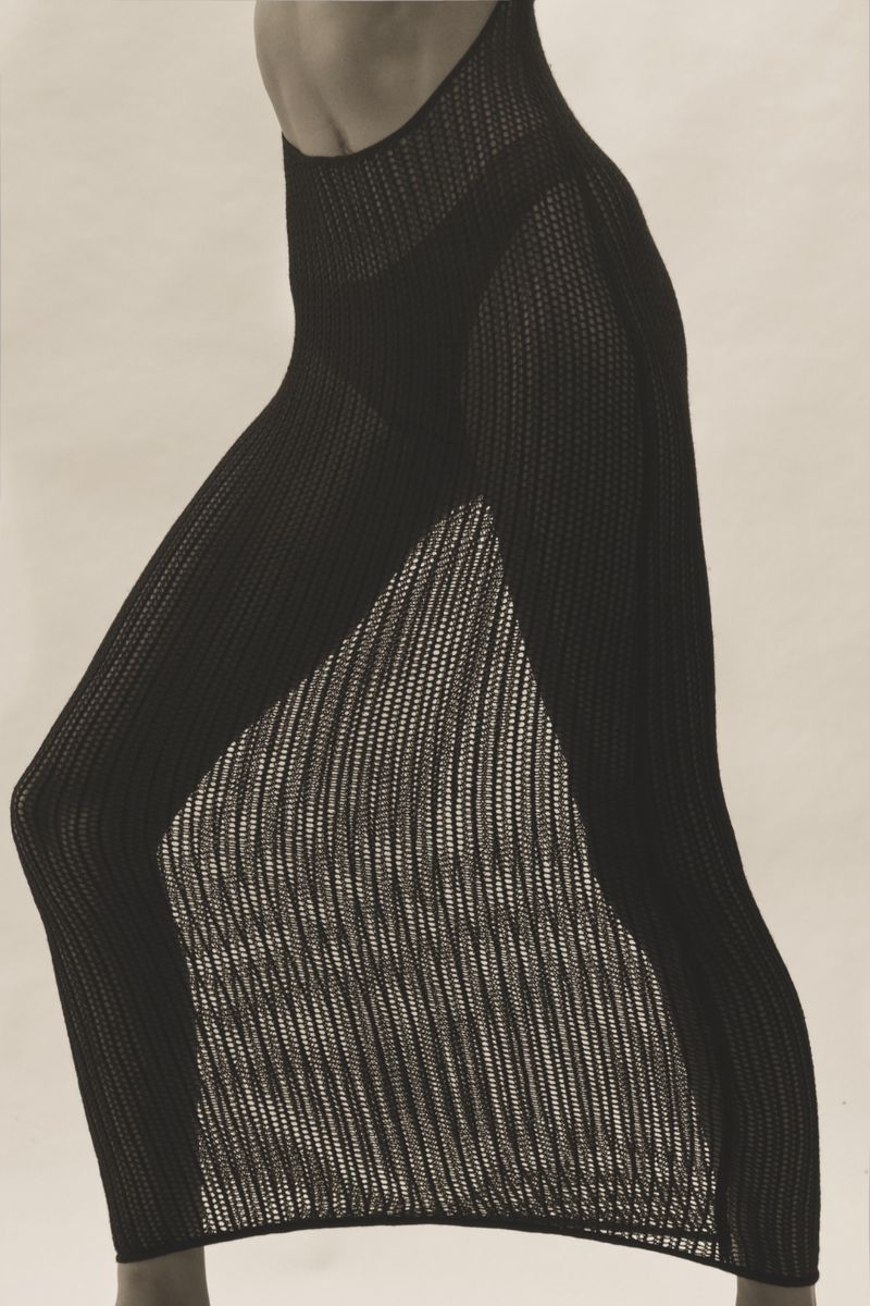 Woman wearing a black knit dress with a slit, captured in a studio setting with soft, diffused lighting, showcasing fashion and style.