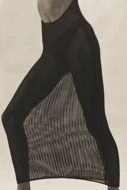 Woman wearing a black knit dress with a slit, captured in a studio setting with soft, diffused lighting, showcasing fashion and style.