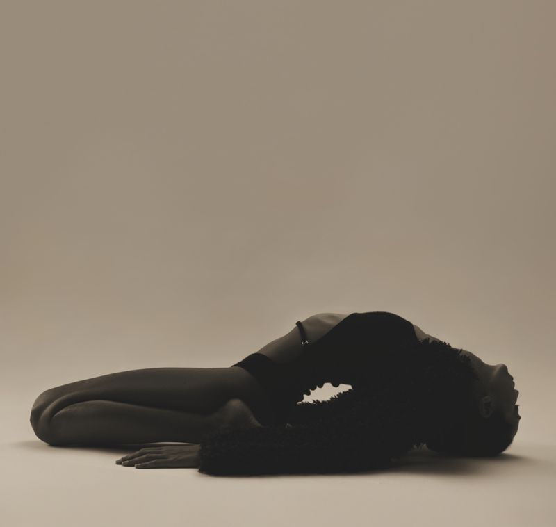 Model lying on studio floor in a dramatic backbend pose wearing black apparel