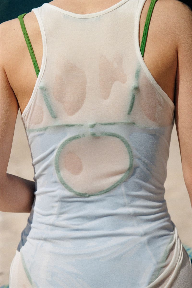 Close-up shot of a woman wearing a white tank top and green bra, showcasing her upper back. The image focuses on fashion.