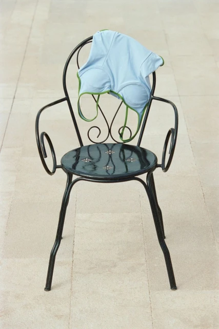 Black metal chair with light-blue tank top draped on it. Neutral background with stone texture. Soft lighting, medium shot.