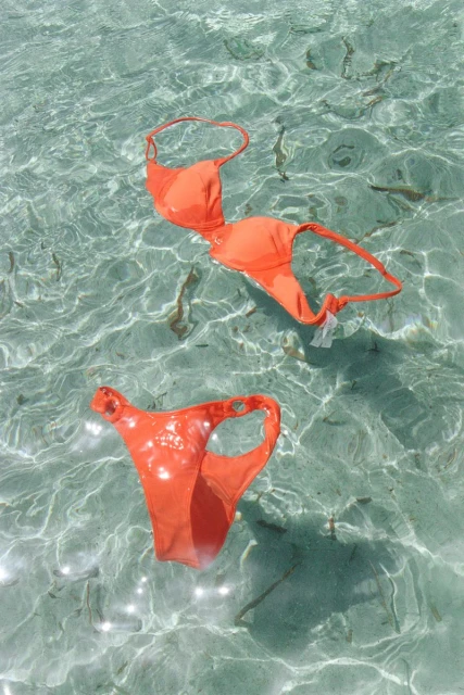 Bright orange bikini set floats in crystal-clear, shallow water, creating a vibrant and playful image for summer fashion or travel themes.
