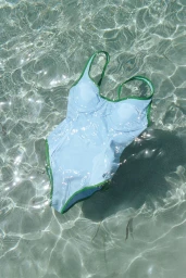 Light blue and green one-piece swimsuit submerged in shallow crystal-clear water with rippling sand beneath.