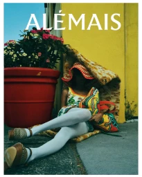 Model wearing patterned dress and white tights seated on pavement next to a large red planter and yellow wall with text ALEMAIS