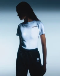 Model wearing a white t-shirt with a black logo and dark trousers against a bright gradient background