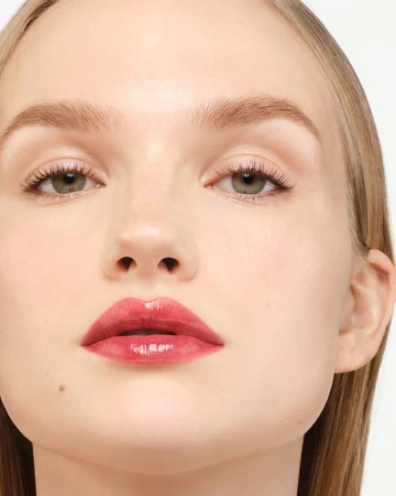 Close-up portrait of a fair-skinned young adult woman with green eyes and light blonde hair, featuring glossy pink lips, against white background.