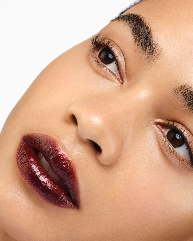 Close-up of a person with dark hair, fair skin, and dark, glossy lips, set against a clean, white background in a beauty context.