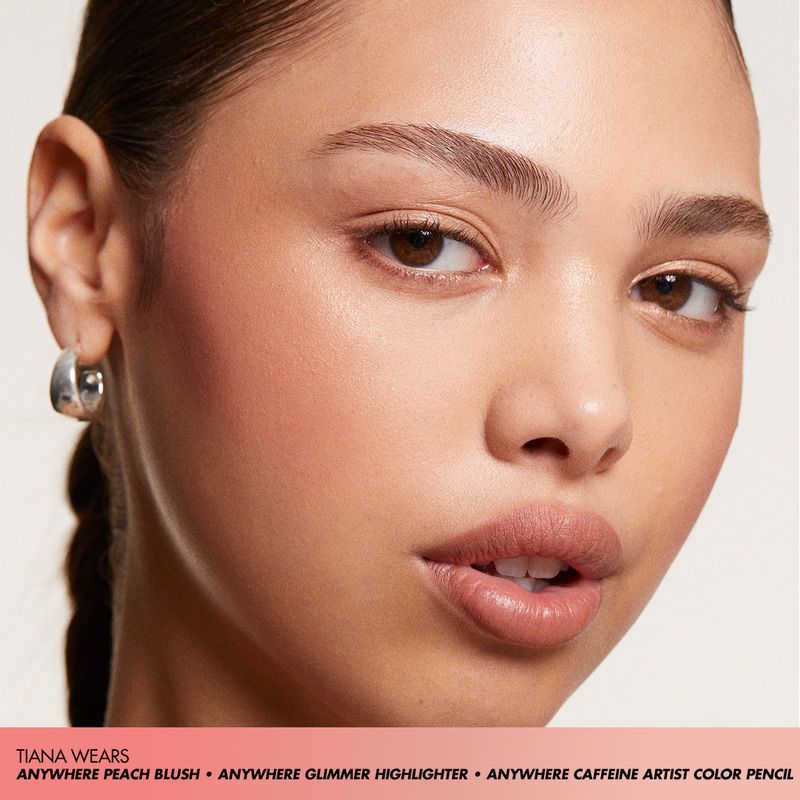 Close-up studio shot of a fair-skinned woman with peach blush, highlighter, and artist color pencil makeup, wearing silver hoop earrings.