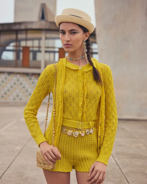Woman in yellow knit shorts suit with Chanel bag poses against architectural backdrop. Fashion editorial shot in natural light.