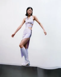 Model in cutout lavender athletic dress and matching knee-high socks standing on a metallic ledge against white