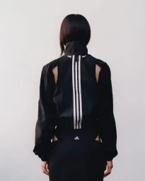 Model seen from the back wearing a black Adidas jacket with white three stripes against a seamless white background.