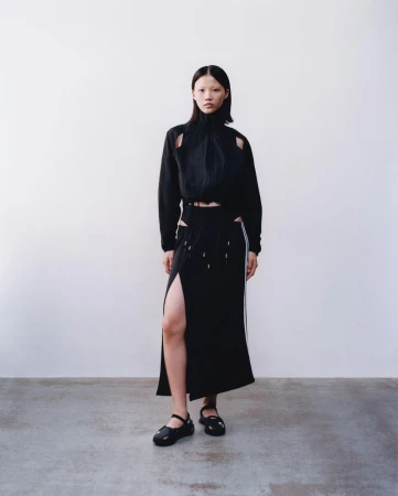 Model in a black cutout top and matching skirt standing against a white backdrop for Adidas