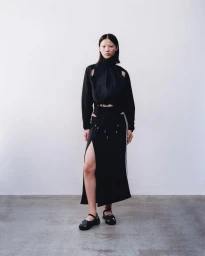 Model in a black cutout top and matching skirt standing against a white backdrop for Adidas