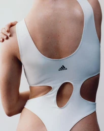 Close-up back view of a model wearing a white athletic bodysuit with cutout details and black Adidas logo for S/S 24