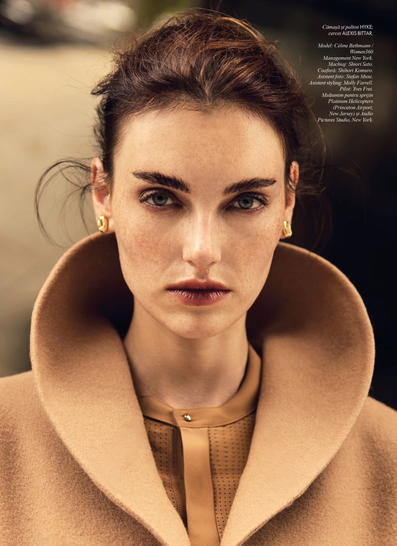 Close-up portrait of a woman with brown hair and neutral makeup wearing a beige coat with a large collar and tan shirt. 