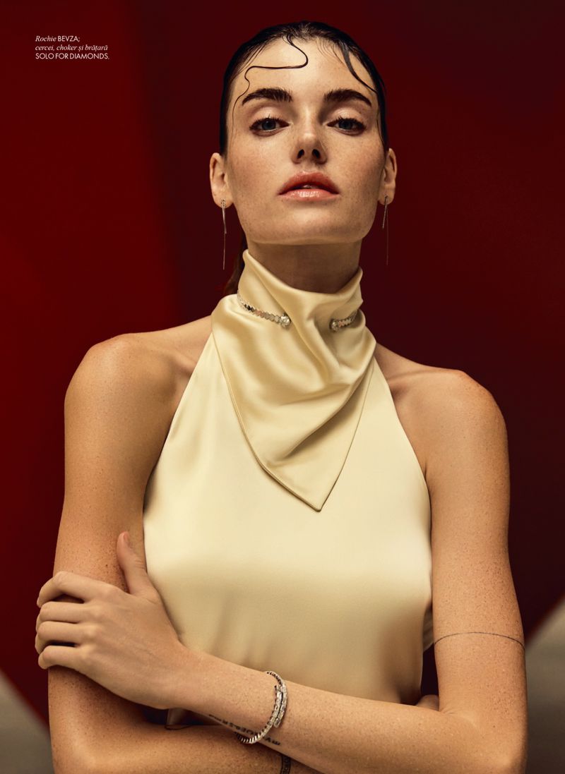 Close-up studio shot of a fair-skinned woman with wet hair, wearing a halter top, jewelry, and neutral makeup against a red backdrop.
