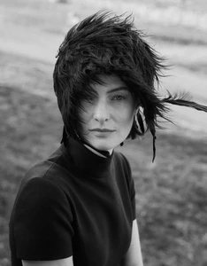 Black and white portrait of a woman with dark short hair and wind-blown bangs wearing a black high-neck top outdoors.