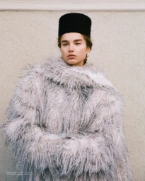 Meghan Roche wearing a fluffy textured coat and black hat against a neutral wall for Vogue Czechoslovakia