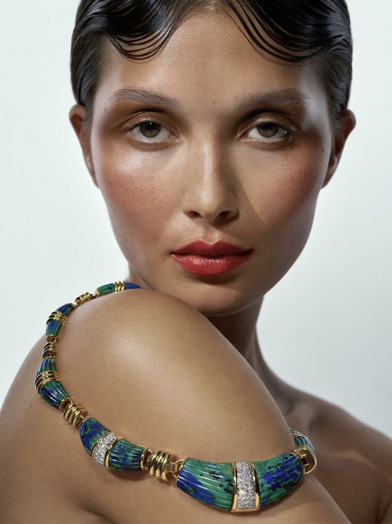 Glamour shot of a woman with an elegant updo and bold red lipstick wearing a chunky necklace with blue and green stones.