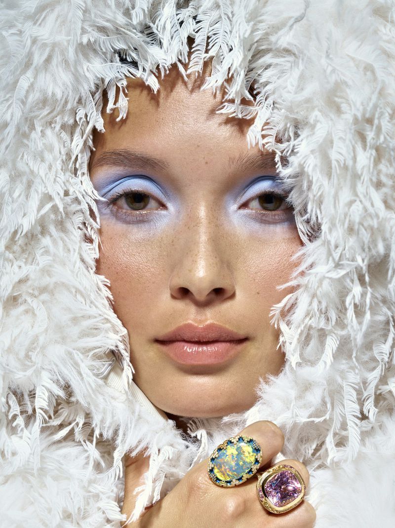 Close-up beauty portrait of model Yada Villaret in a textured white fringe hood with pastel blue eyeshadow and statement rings.