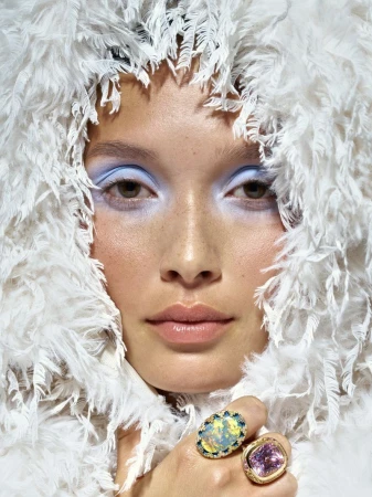 Close-up beauty portrait of model Yada Villaret in a textured white fringe hood with pastel blue eyeshadow and statement rings.