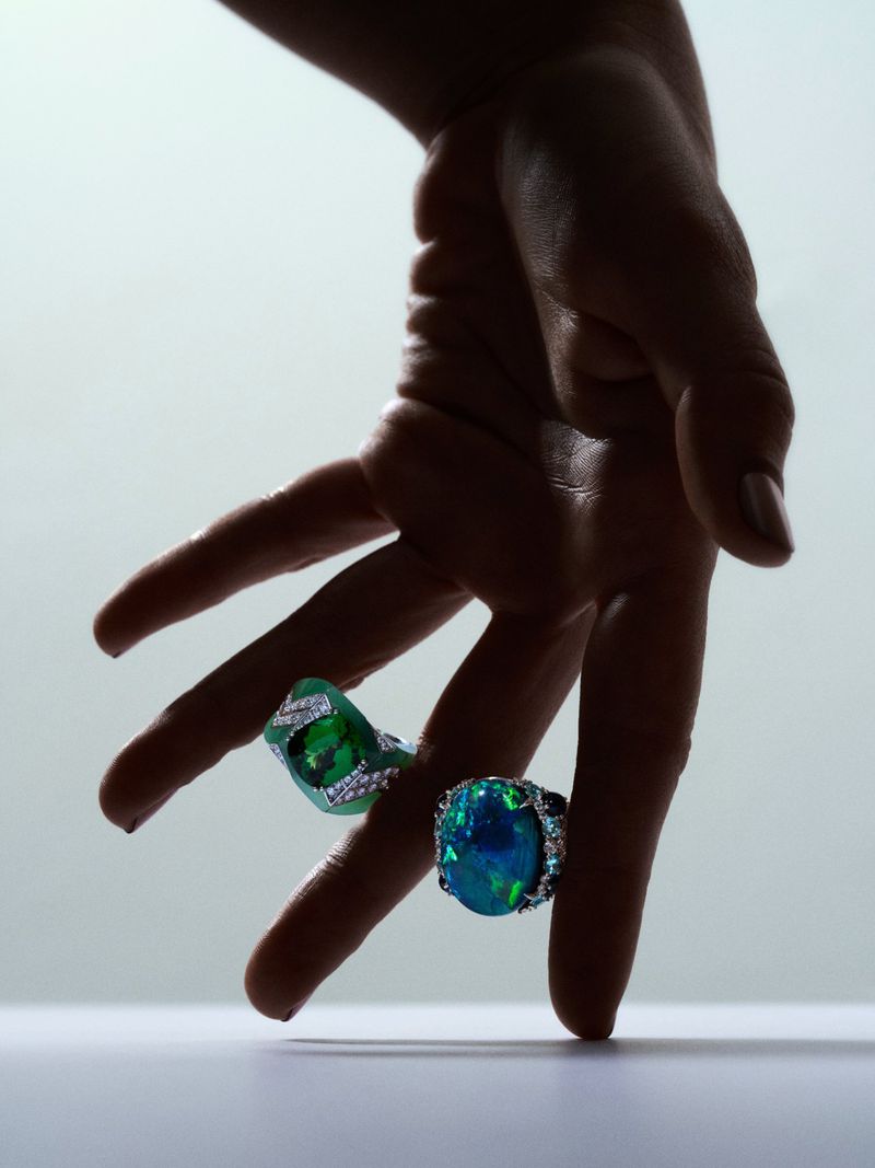 Close-up of a hand holding jewelry rings with various gems against a soft gradient background in a studio setting.