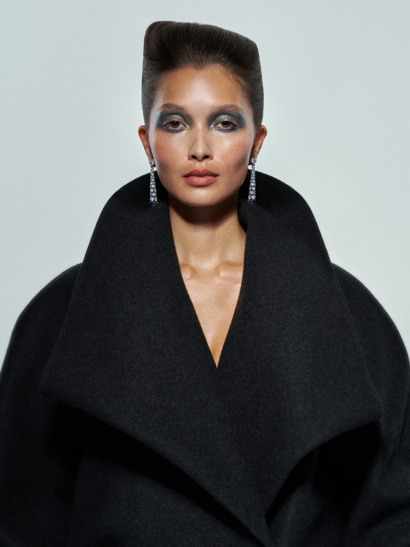 Portrait of a model in a black coat with a high collar against a white background, showcasing fashion and beauty elements.