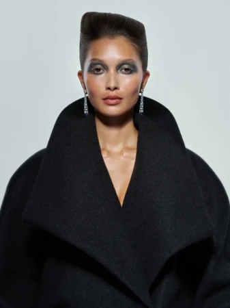 Portrait of a model in a black coat with a high collar against a white background, showcasing fashion and beauty elements.