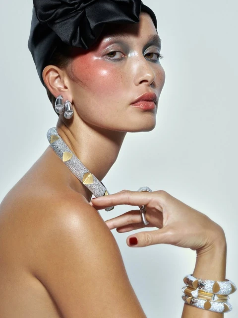 Portrait of a woman wearing a black headscarf, sparkling choker necklace, and matching bracelets against a neutral backdrop in a studio.