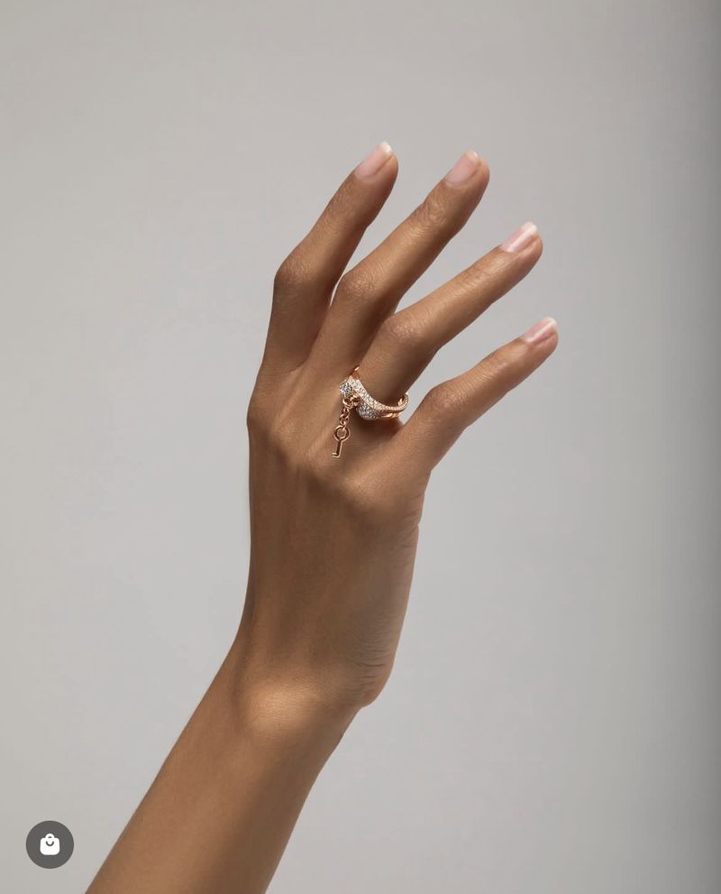 Woman's hand displaying an elegant gold ring with sparkling accents and a dangling key charm against a soft, neutral background.