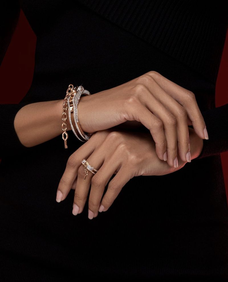 Close-up of woman's hands adorned with bracelets and ring featuring key charms against a dark backdrop, showcasing fashion jewelry.