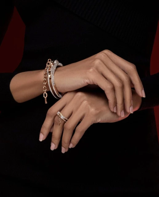 Close-up of woman's hands adorned with bracelets and ring featuring key charms against a dark backdrop, showcasing fashion jewelry.