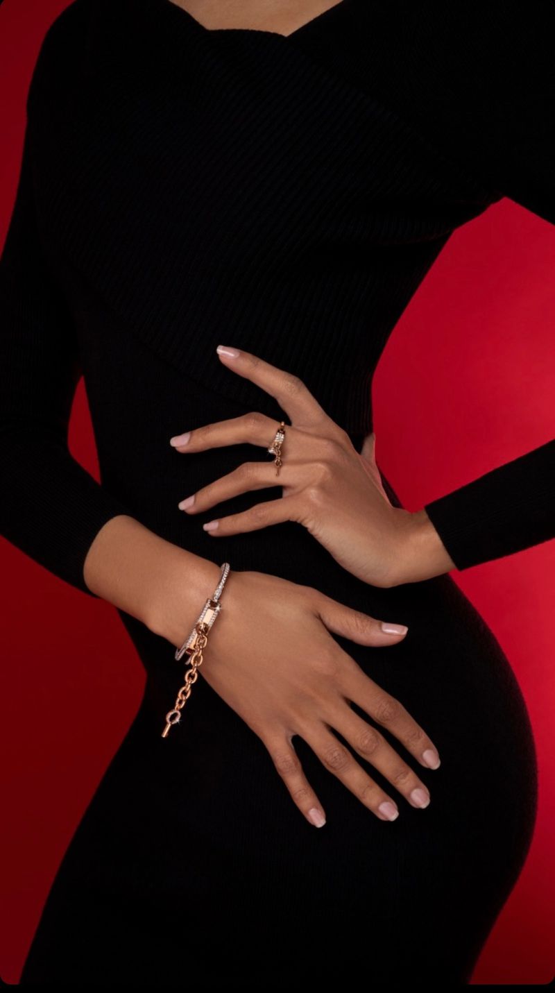 Woman in black dress posing with jewellery on wrist and finger in front of a red background. Beauty and fashion product shot.