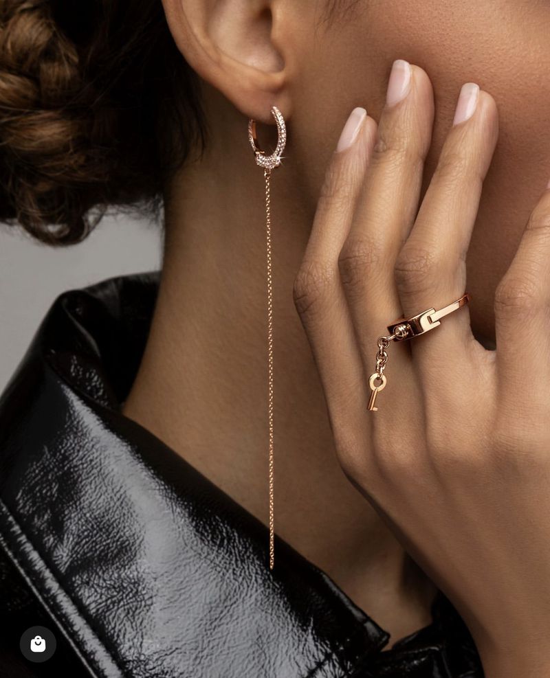 Close-up of an adult female wearing rose gold hoop earrings and a ring with a key pendant, showcasing jewelry design and fashion.