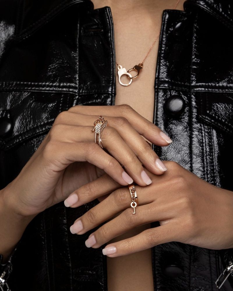 Close-up studio shot of a light-skinned human wearing gold jewelry: rings on the right hand and a handcuff pendant necklace.
