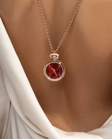 Close up of a rose gold necklace with a red watch pendant worn against a model's back in a white silk dress