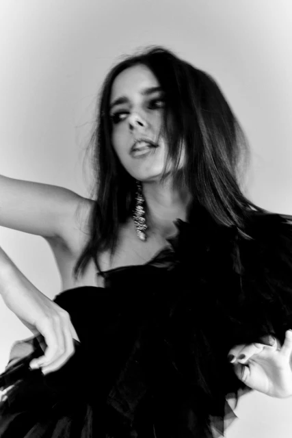 Black and white portrait of a woman in a feather boa looking up with dark hair and dangling earrings against a plain backdrop.