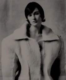 Monochrome portrait of a woman with short dark hair wearing an oversized structured wool coat against a textured studio backdrop.