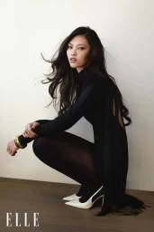 Model May Li Wescott crouching in a black dress and white heels for an Elle China editorial shoot against a neutral wall