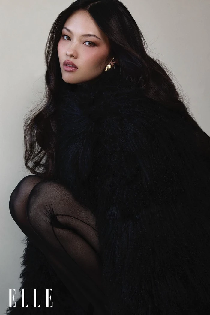 Model May Li Wescott wearing a voluminous black feathered coat and sheer black tights against an off-white background for Elle China.