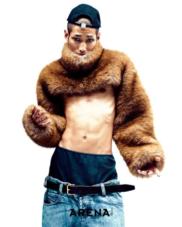 Male fashion model posing in denim jeans and fur collar shrug with backwards hat in a bright studio setting for editorial work.