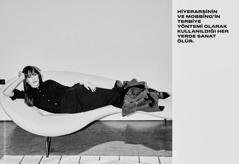 Monochrome fashion shot of a woman lying on a curved white couch with a patterned jacket, against a plain background with text.