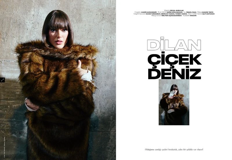 Fashion editorial featuring a woman with bangs in a large brown fur coat, standing against a textured gray wall with neutral studio lighting.