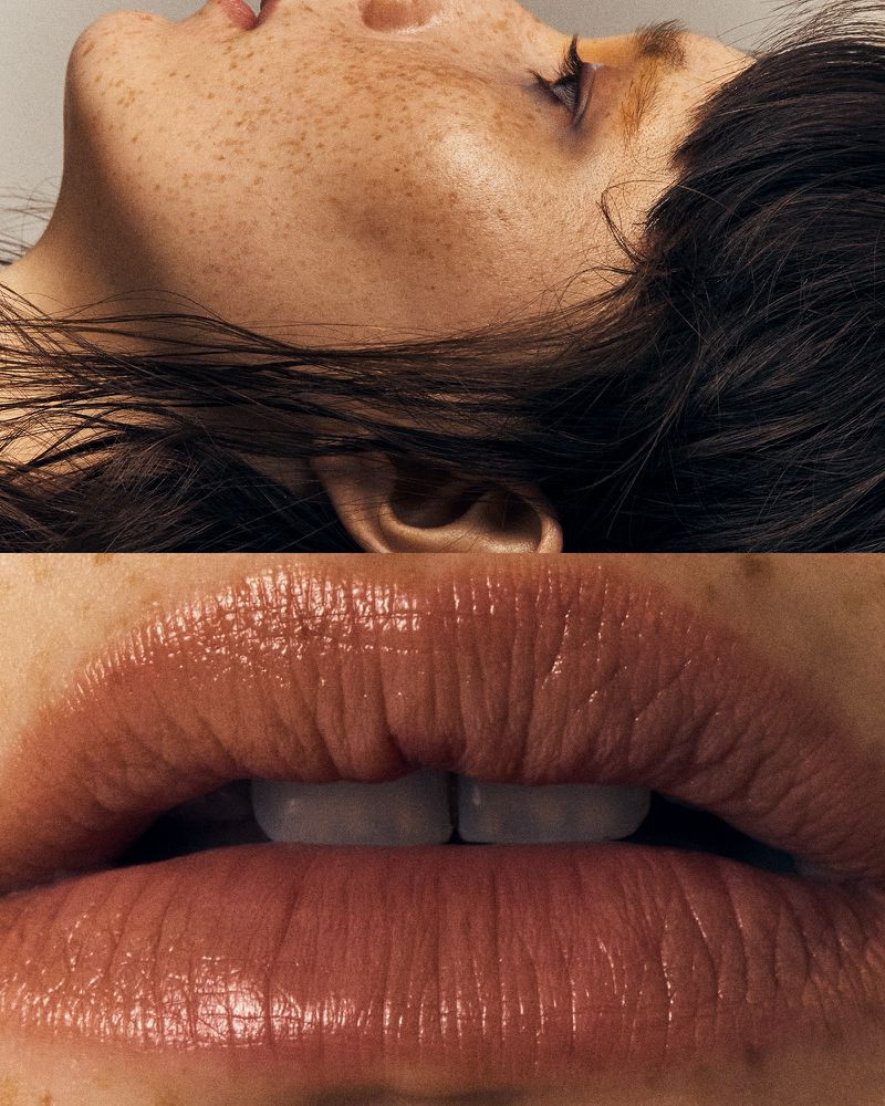 Close-up of a woman's face, showcasing freckled skin, brown hair, and glossy lips in a beauty or skincare context. Focus on detail.
